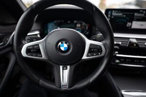 Close-up of a BMW car steering wheel, perfect for your Las Vegas adventure. The black leather cover with silver accents and the iconic BMW logo make it irresistible. Various control buttons grace the sides, while the dashboard and infotainment screen offer electronic displays. Experience luxury at affordable rental rates.